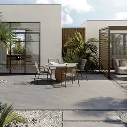 An outdoor patio area with large grey floor tiles that have a natural stone appearance. The space features modern outdoor furniture, including a round dining table with chairs and a lounging area. The clean lines and neutral tones of the tiles complement the sleek architectural elements and lush greenery surrounding the patio.