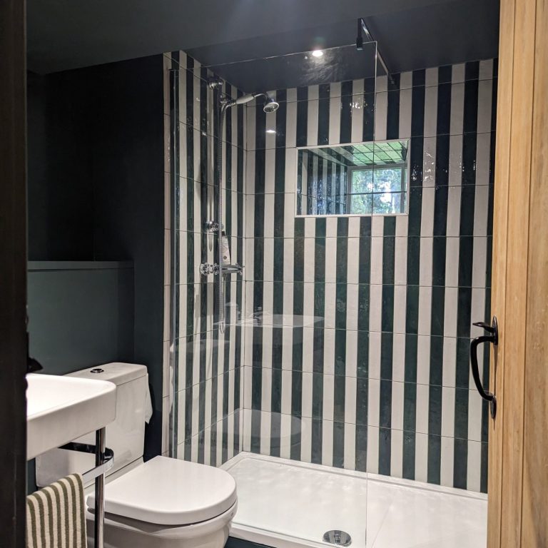 Vertical Striped Tiles: The tiles in the shower area are arranged in bold vertical stripes, alternating between dark and light shades. This pattern not only adds a dramatic visual effect but also creates an illusion of height, making the bathroom appear taller and more spacious.