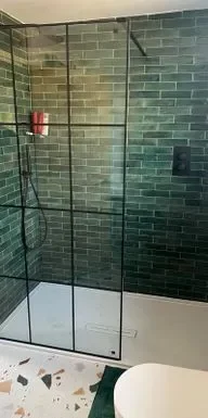 Modern bathroom featuring a sleek glass shower enclosure with black framing and stylish green subway tiles, paired with a contemporary white floor showcasing unique terrazzo patterns.