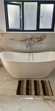 Luxurious bathroom featuring a white freestanding bathtub with a modern design, set against elegant marble effect tiles and a large window, creating a serene and spa-like ambiance.